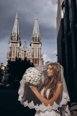 Gelinlik giymiş çekici genç gelin elinde bir buket çiçekle şehirde       