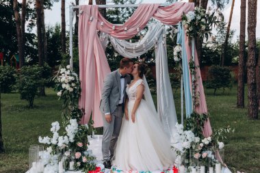 Düğün kemerinin yanında poz veren mutlu gelin ve damat parktaki düğün töreninde            