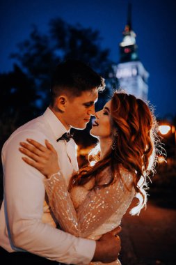 Düğün çifti gece şehrinin arka planında öpüşüyor.