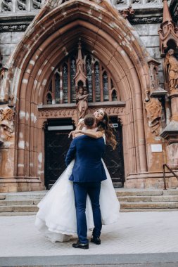 Mutlu genç damat düğün günü kilisenin yanında çekici gelini kucaklıyor ve taşıyor.          