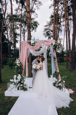 Düğün kemerinin yanında poz veren mutlu gelin ve damat parktaki düğün töreninde            