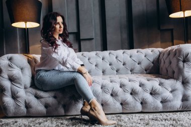 Stüdyoda gri koltukta poz veren güzel esmer kadın.