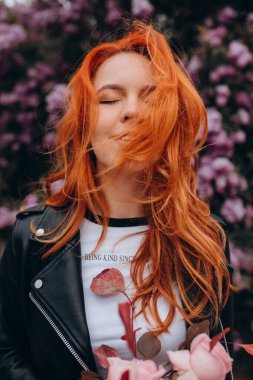 Parkta çiçek açan ağaca poz veren güzel kızıl saçlı kız.