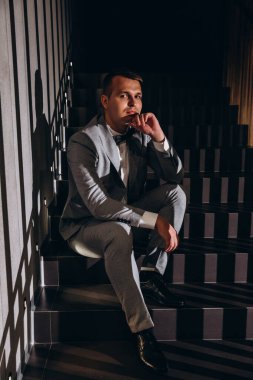 Takım elbiseli genç adamın portresi merdivenlerde oturuyor ve başka tarafa bakıyor. 