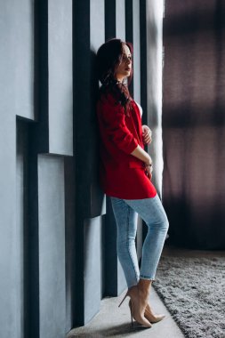 Kırmızı ceketli güzel esmer kadın odada poz veriyor. 