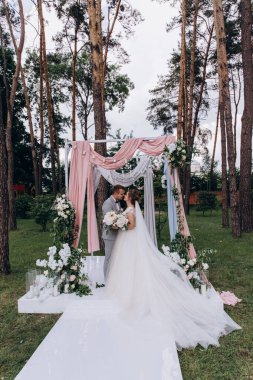 Düğün kemerinin yanında poz veren mutlu gelin ve damat parktaki düğün töreninde            