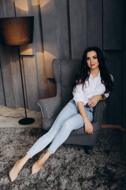 Beyaz gömlekli ve kot pantolonlu genç bir kadın stüdyoda poz veriyor. 