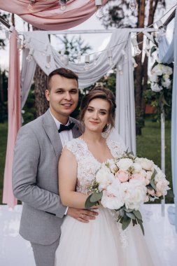 Düğün kemerinin yanında poz veren mutlu gelin ve damat parktaki düğün töreninde            