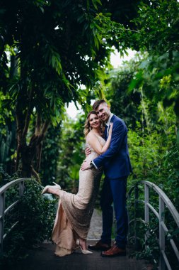 Mutlu gelin ve damat botanik bahçesinde köprüde kucaklaşıyor. 