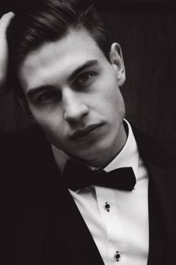 Takım elbiseli ve papyonlu yakışıklı bir gencin portresi. Siyah beyaz kameraya bakıyor.