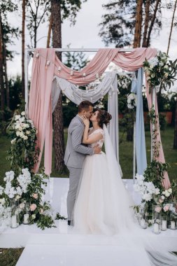 Düğün kemerinin yanında poz veren mutlu gelin ve damat parktaki düğün töreninde            