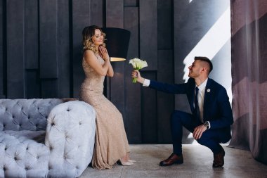 Genç çift düğün günlerinde stüdyoda poz verirken damat gelinine bir buket beyaz çiçek verir. 