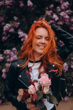 Parkta çiçek açan ağaca poz veren güzel kızıl saçlı kız.