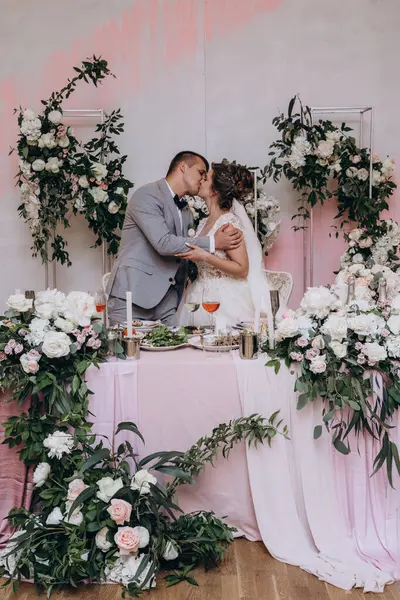 Mutlu genç gelin ve damat restoranda masada öpüşüyor.