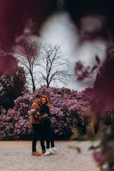 Genç ve güzel bir çift çiçek açan çalılara karşı poz veriyor. 