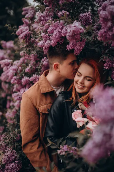 Mutlu çift arka planda çiçeklerle poz veriyor. 