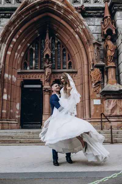 Mutlu genç damat düğün günü kilisenin yanında çekici gelini kucaklıyor ve taşıyor.          
