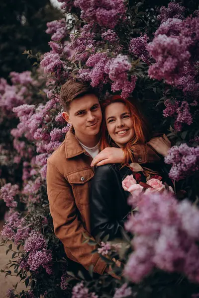 Mutlu çift arka planda çiçeklerle poz veriyor. 