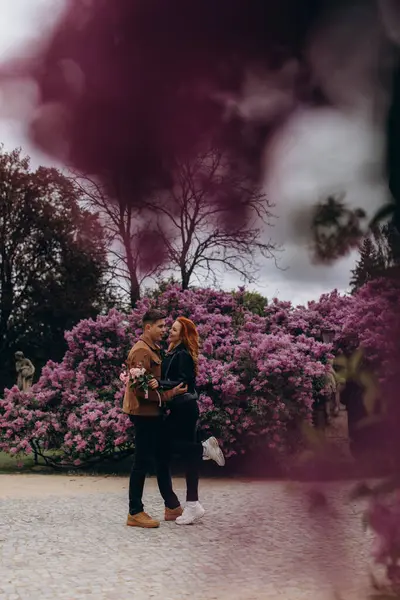 Genç ve güzel bir çift çiçek açan çalılara karşı poz veriyor. 