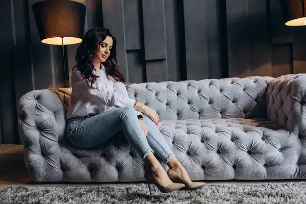 Stüdyoda gri koltukta poz veren güzel esmer kadın.