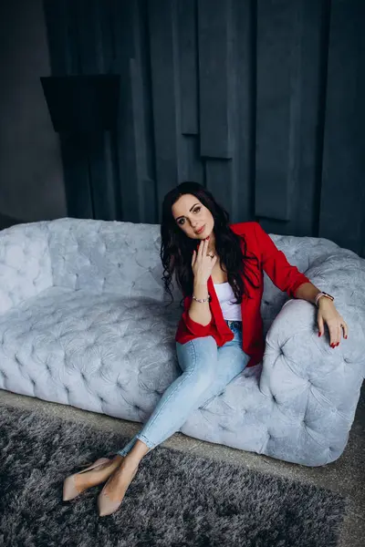 Genç, güzel, esmer, kırmızı ceketli kadın kanepede oturuyor. 