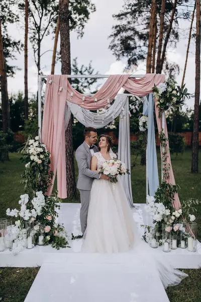 Düğün kemerinin yanında poz veren mutlu gelin ve damat parktaki düğün töreninde            