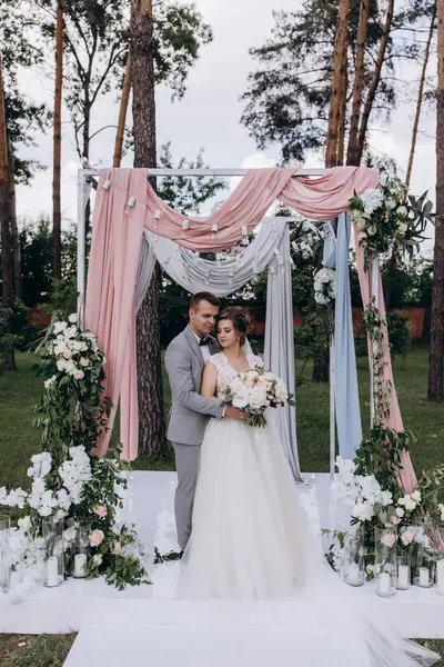 Düğün kemerinin yanında poz veren mutlu gelin ve damat parktaki düğün töreninde            