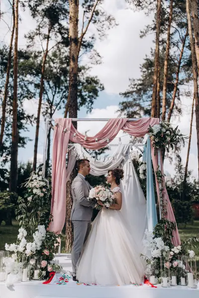 Düğün kemerinin yanında poz veren mutlu gelin ve damat parktaki düğün töreninde            