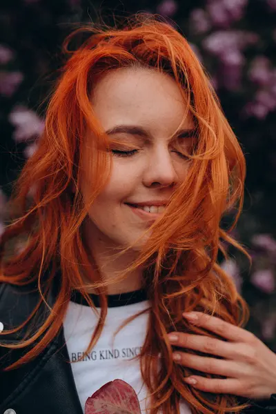 Parkta çiçek açan ağaca poz veren güzel kızıl saçlı kız.