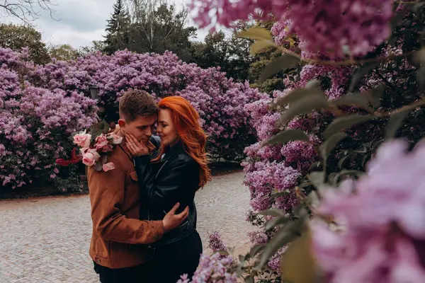 Genç ve güzel bir çift çiçek açan çalılara karşı poz veriyor. 