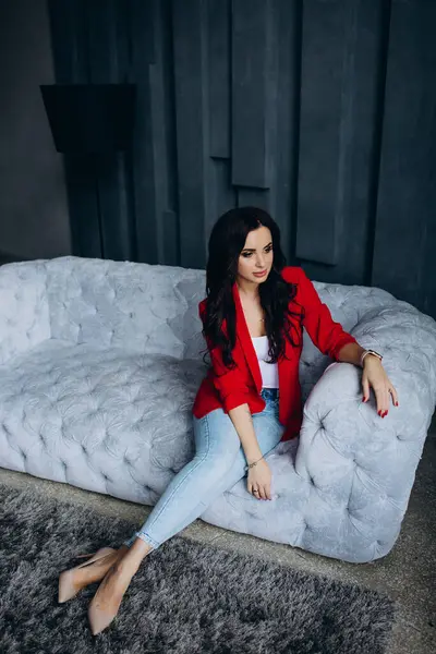 Genç, güzel, esmer, kırmızı ceketli kadın kanepede oturuyor. 