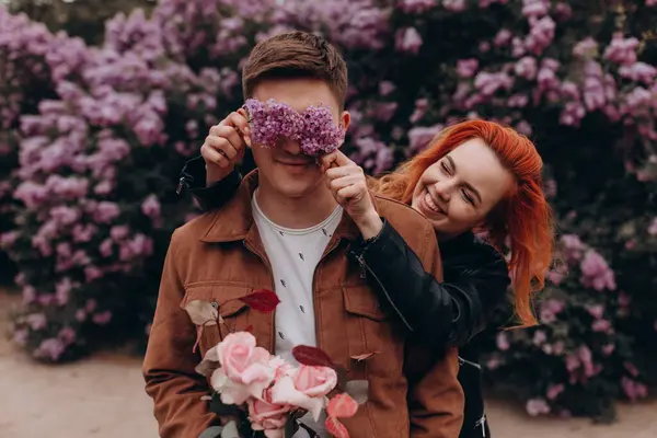 Mutlu çift arka planda çiçeklerle poz veriyor. 