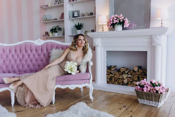 Parlak elbiseli mutlu genç kadın stüdyodaki pembe kanepede yatıyor.