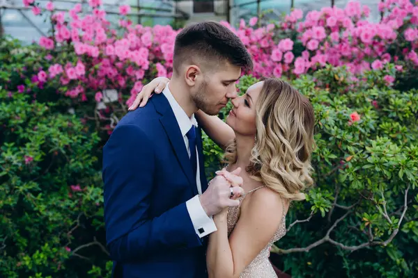 Zarif genç çiftin el ele tutuşup bahçede kucaklaşmalarının yan görüntüsü.