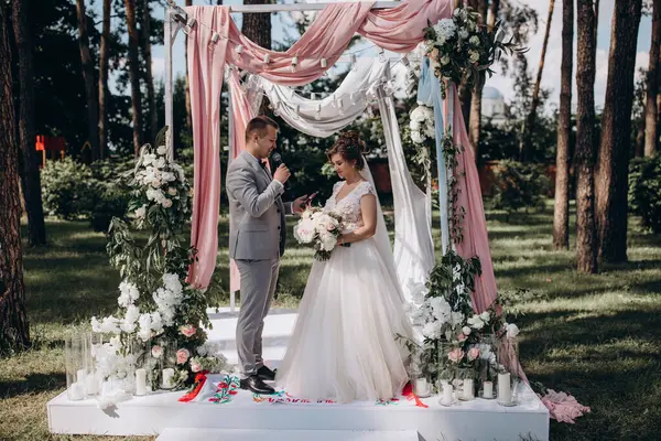 Düğün kemerinin yanında poz veren mutlu gelin ve damat parktaki düğün töreninde            