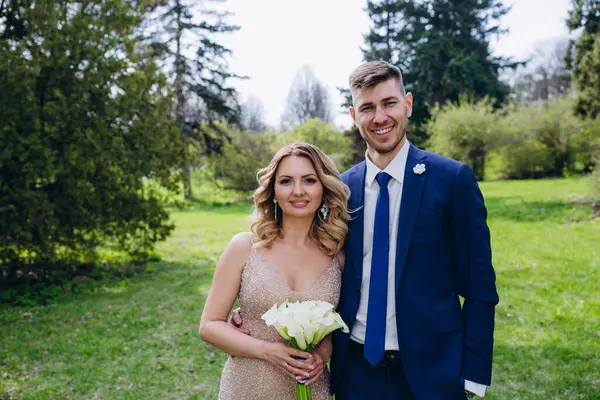 Mutlu genç gelin ve damat parkta kameraya gülümsüyor.