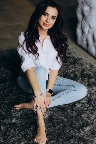 Beyaz gömlekli ve kot pantolonlu genç bir kadın stüdyoda poz veriyor. 