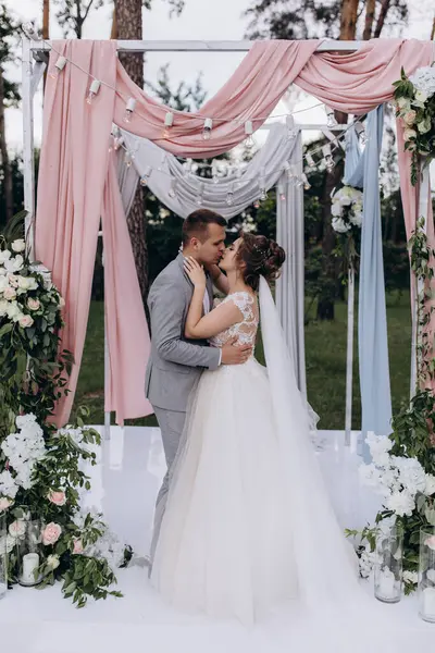 Düğün kemerinin yanında poz veren mutlu gelin ve damat parktaki düğün töreninde            