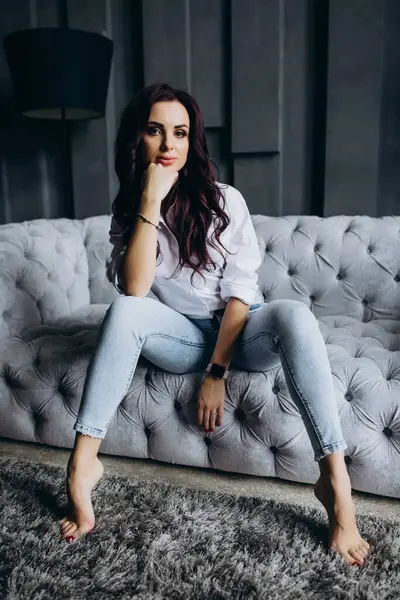 Beyaz gömlekli ve kot pantolonlu genç bir kadın stüdyoda poz veriyor. 