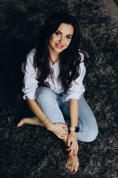 Beyaz gömlekli ve kot pantolonlu genç bir kadın stüdyoda poz veriyor. 