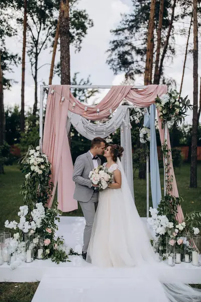 Düğün kemerinin yanında poz veren mutlu gelin ve damat parktaki düğün töreninde            