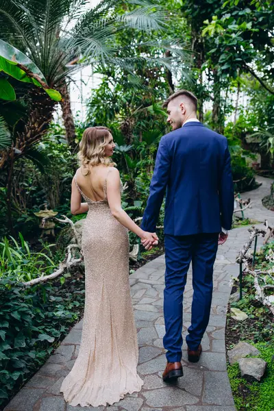 Güzel genç çift palmiye ağaçlarının arka planında botanik bahçesinde yürüyor ve poz veriyor..