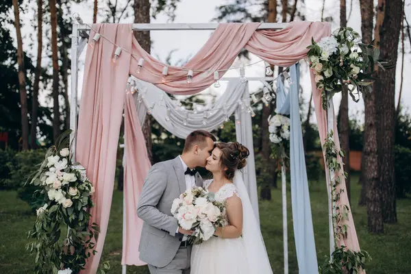 Düğün kemerinin yanında poz veren mutlu gelin ve damat parktaki düğün töreninde            