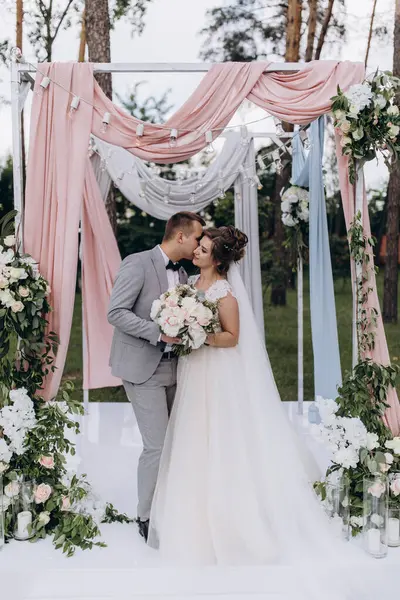 Düğün kemerinin yanında poz veren mutlu gelin ve damat parktaki düğün töreninde            