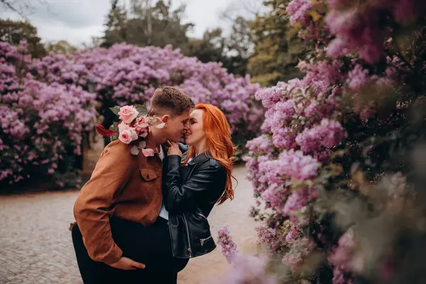 Genç ve güzel bir çift çiçek açan çalılara karşı poz veriyor. 