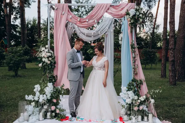 Düğün kemerinin yanında poz veren mutlu gelin ve damat parktaki düğün töreninde            