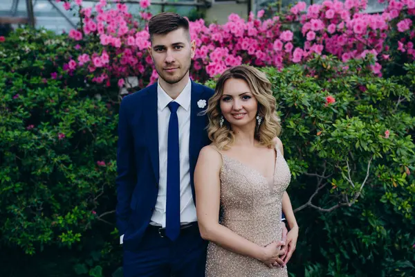 Mutlu gelin ve damat, botanik bahçesinde mor çiçeklerin önünde köprüde kucaklaşıyorlar. 