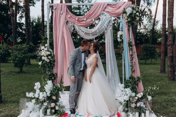 Düğün kemerinin yanında poz veren mutlu gelin ve damat parktaki düğün töreninde            