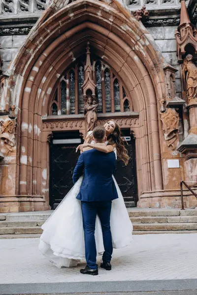 Mutlu genç damat düğün günü kilisenin yanında çekici gelini kucaklıyor ve taşıyor.          