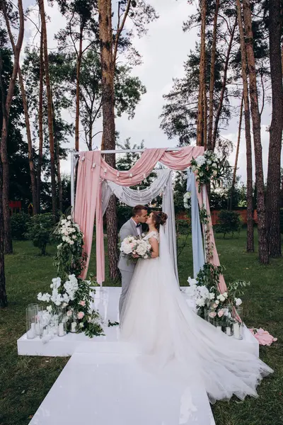 Düğün kemerinin yanında poz veren mutlu gelin ve damat parktaki düğün töreninde            